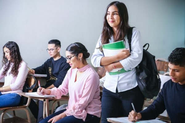 classroom with students and a student with a backpack standing up with papers - Photo by javier trueba on Unsplash